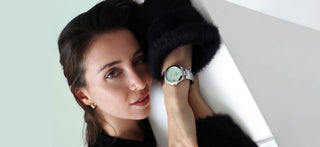 Woman wearing a Swiss COVER Iconosteel Lady watch with a light green face on a plain background